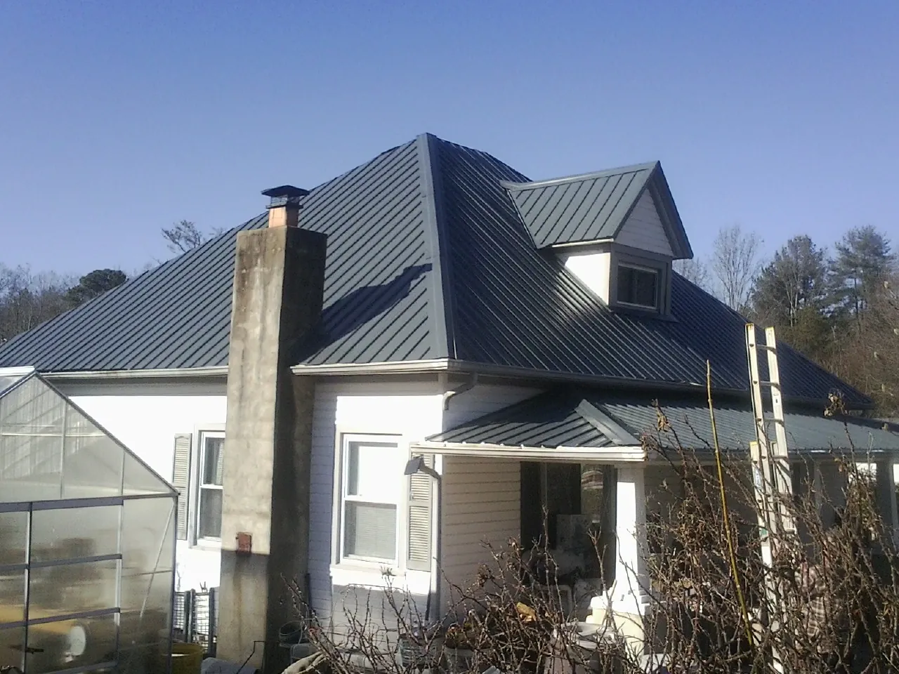 Dark blue standing seam metal roof on a white farmhouse with dormer — Slate & Tile Roof Repair by Roofing Brothers in Lees Summit