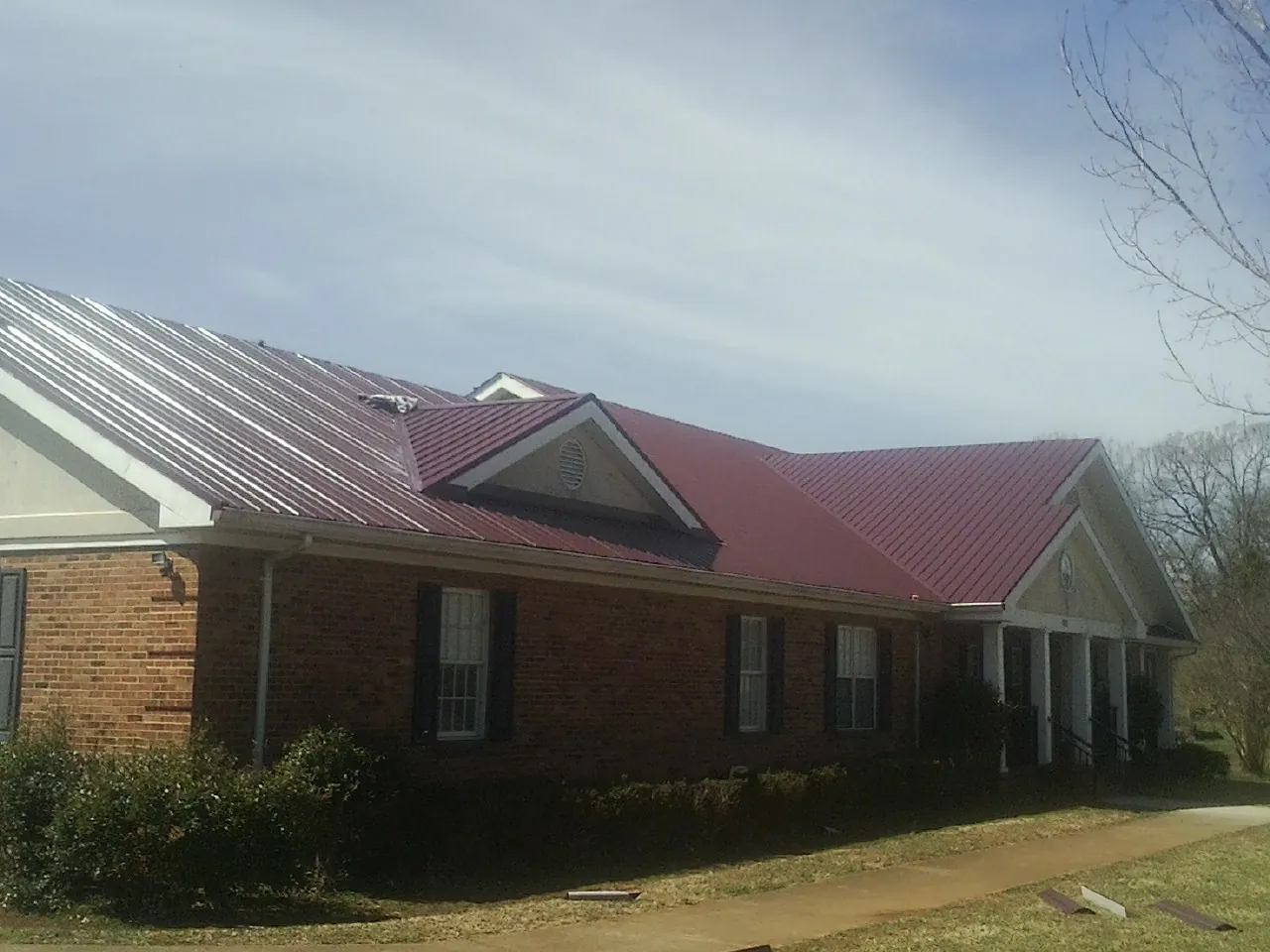 Red metal roof with gabled entries on a long brick building, from a Hail Damage Roof Repair job in Lees Summit