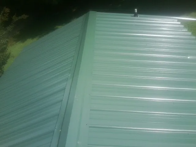 New green metal panels meeting at the ridge of a roof — Flat Roof Repair work by our crew in Lees Summit