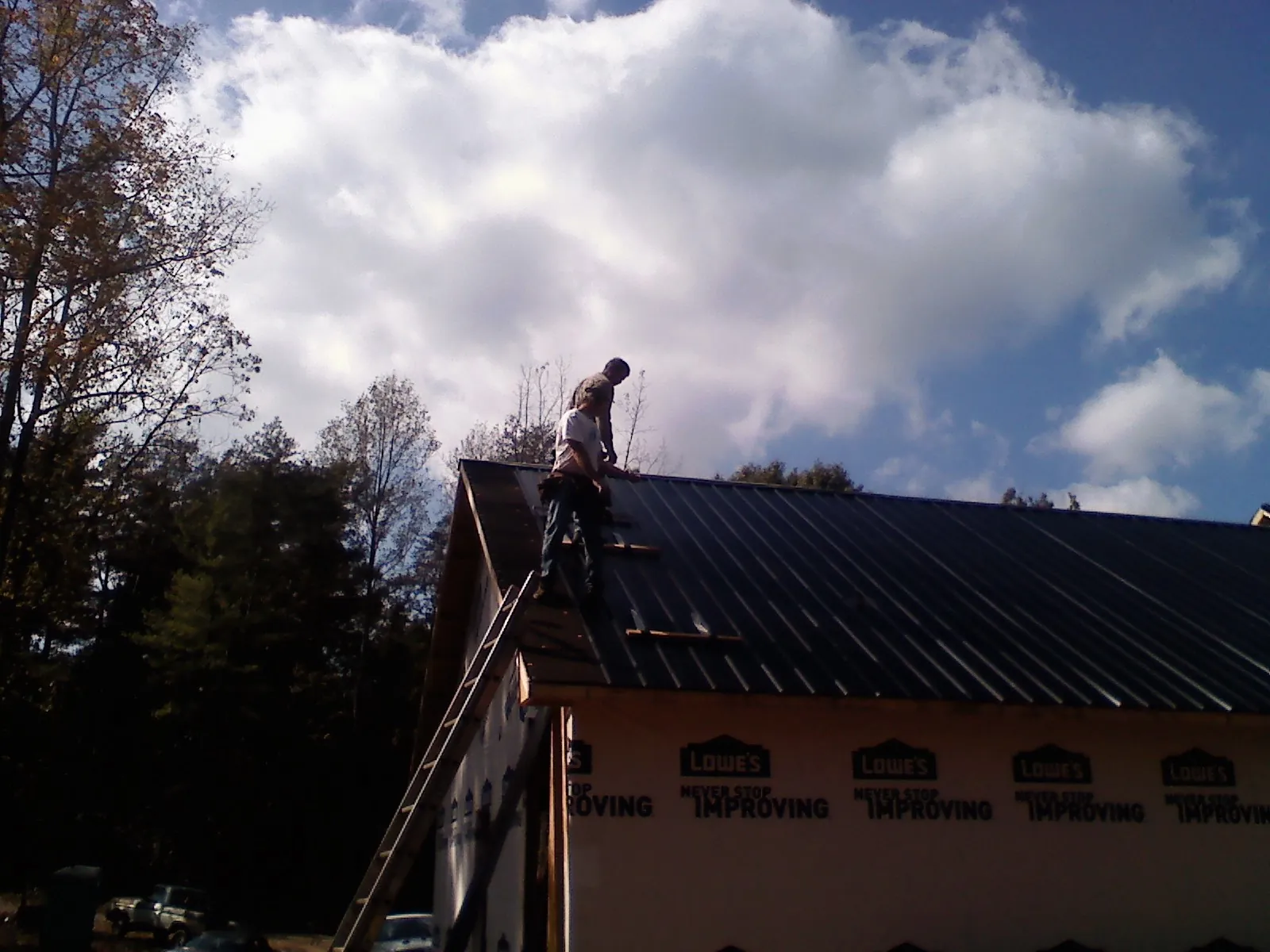 Roofer fastening dark metal panels high against a cloudy sky, from a Roof Inspection job in Lees Summit