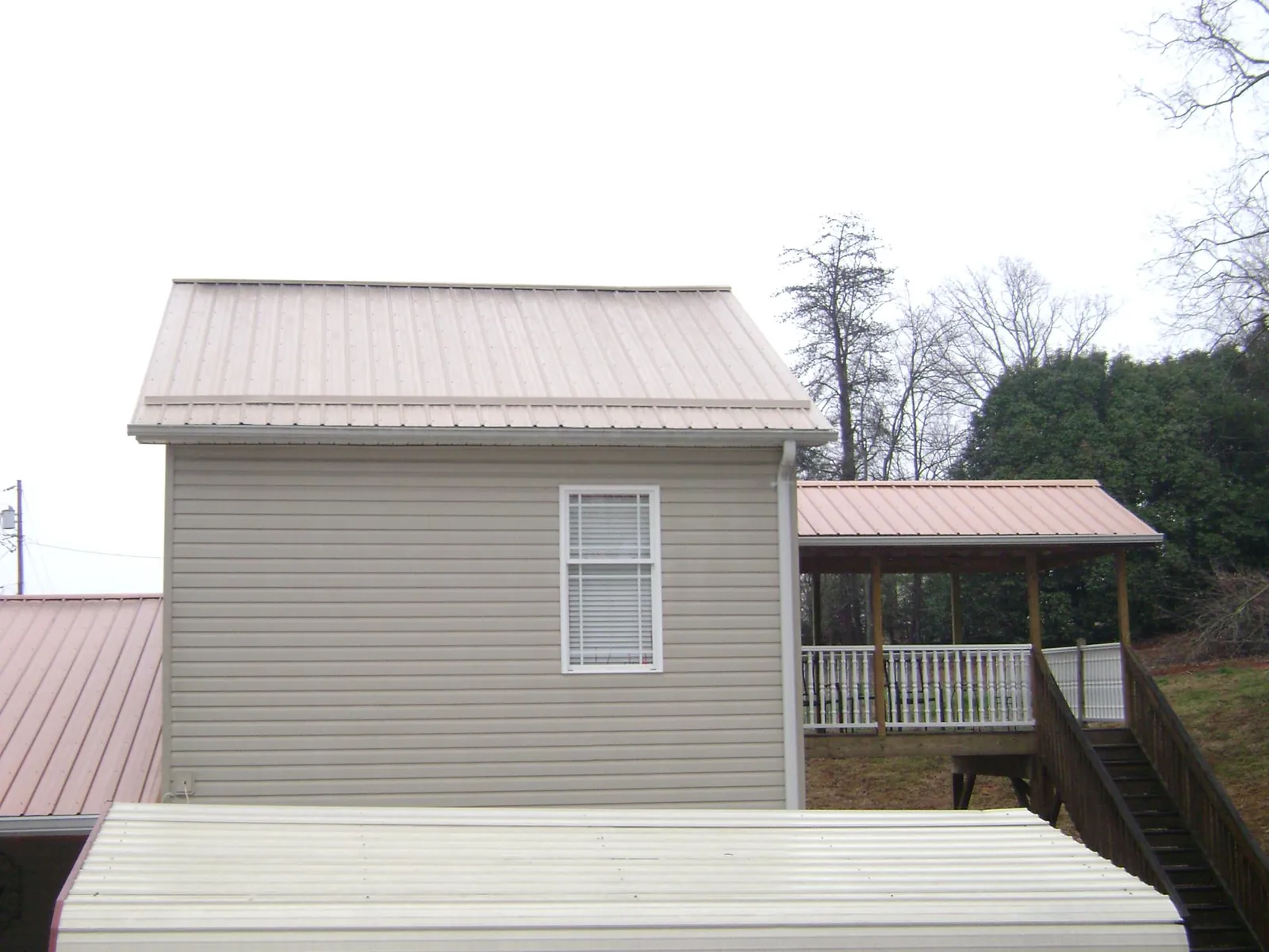 Tan metal roofs on a two story addition and attached porch, from a Roof Replacement job in Lees Summit